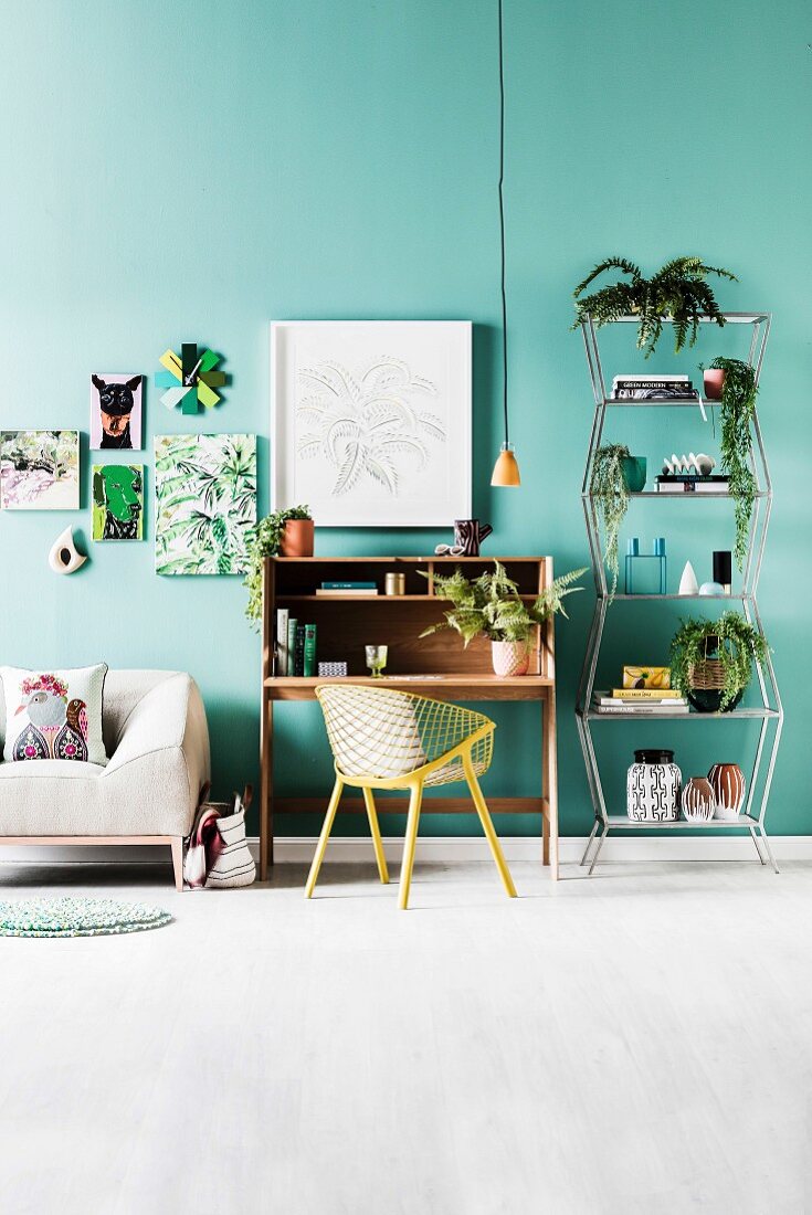Sofa, Sekretär mit Schalenstuhl und Metallregal mit Zimmerpflanzen, an grüner Wand Bilder mit Pflanzen- und Tiermotiven