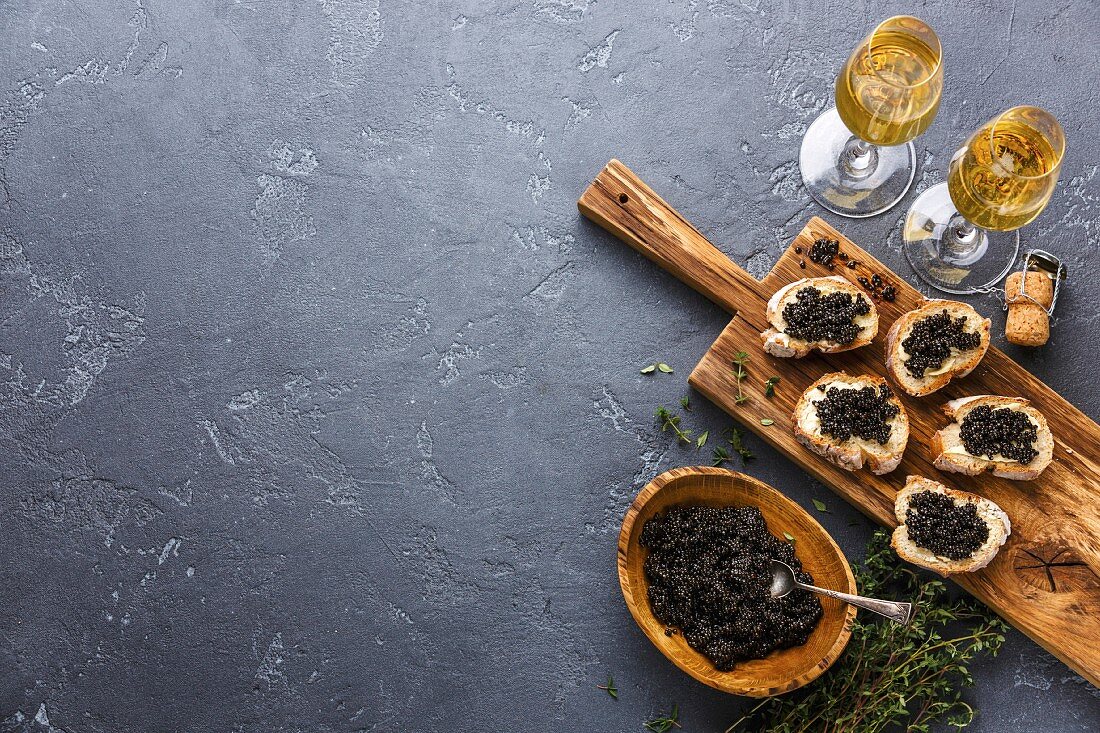 Schwarzer Kaviar in Holzschale und auf Brot, dazu Champagner