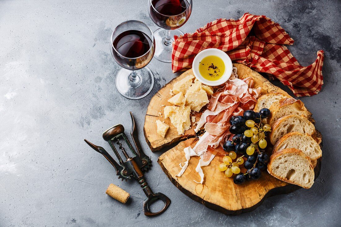 Vorspeisenplatte mit Schinken, Parmesan, Trauben, Brot und Rotwein