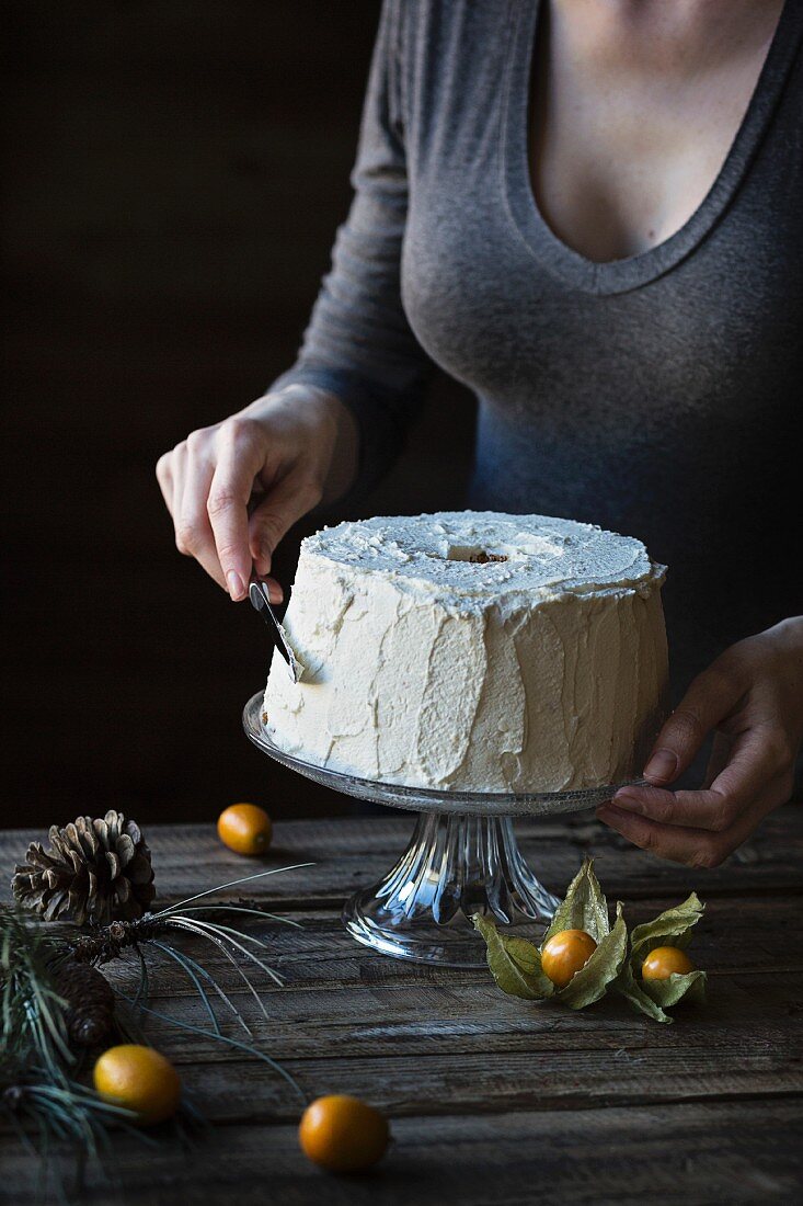 Woman is frosting a chiffon cake on wooden table
