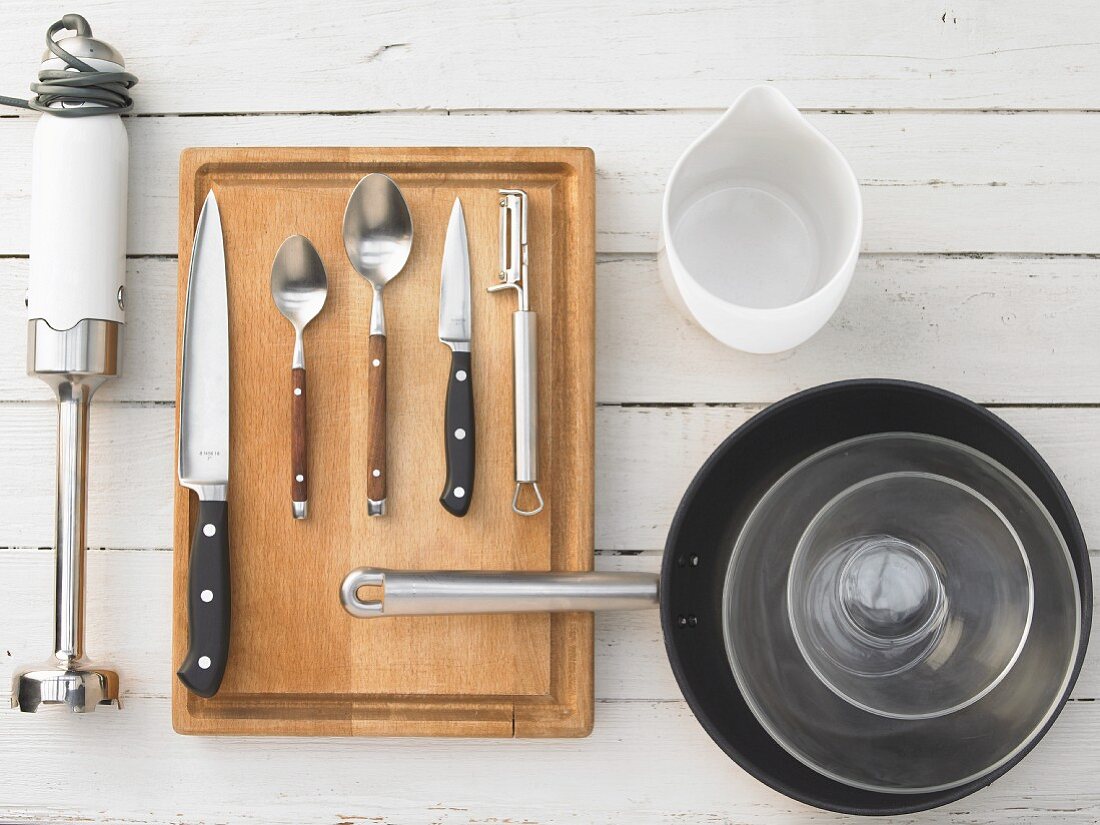 Verschiedene Küchenutensilien: Pürierstab, Messer, Löffel, Pfanne, Glasschalen