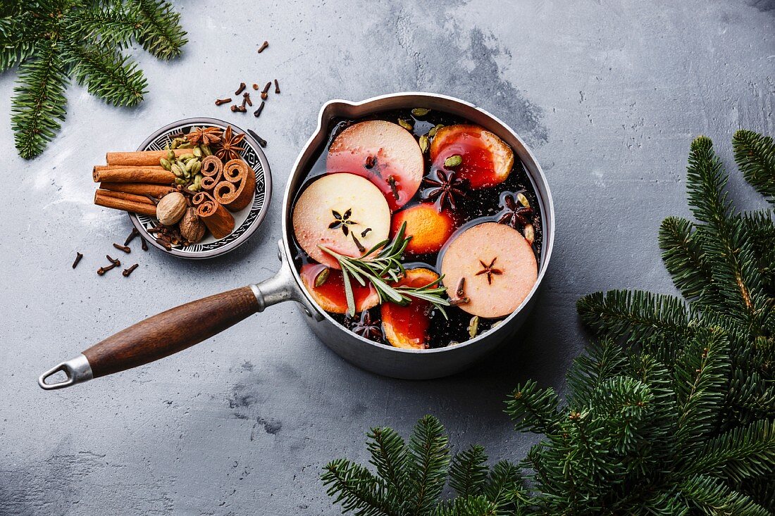 Glühwein mit Orangen, Äpfeln und Gewürzen in Aluminiumtopf