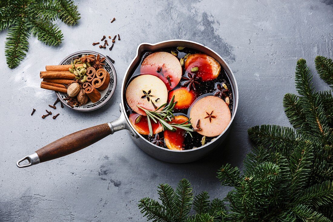 Mulled wine hot drink with citrus, apple and spices in aluminum casserole and Fir branch