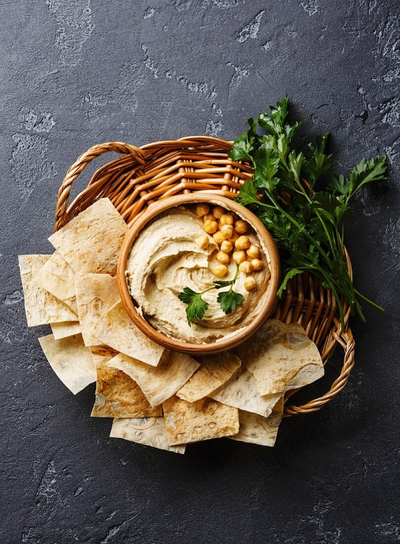 Homemade hummus with pita chips and parsley on black stone background copy space