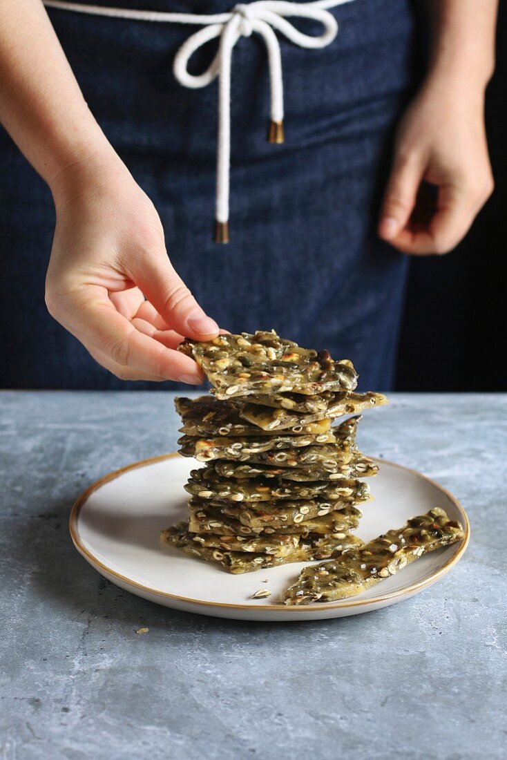 Female hand staking pieces of pumpkin seed brittle on a plate