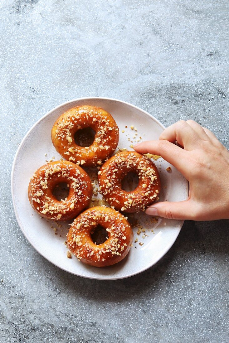 Female hand grabbing a donut with honey maple syrup and ground walnuts from a plate, top view