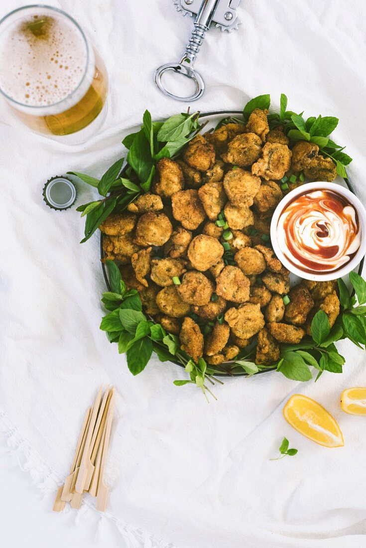 Fried pickles accompanied by a ketchup and mayonnaise sauce and a glass of beer photographed from top view