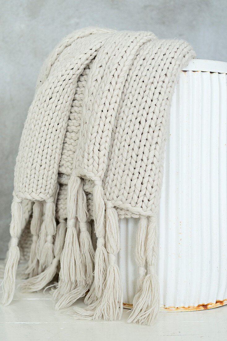 Pale knitted blanket in white metal bin