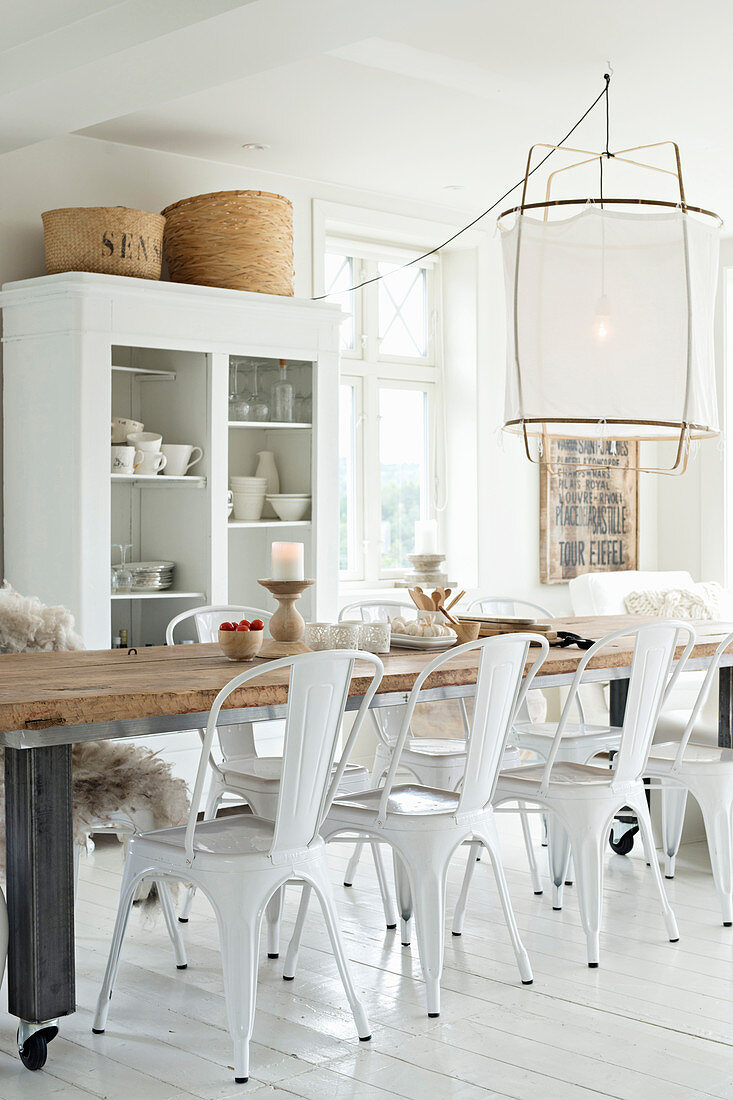 Long dinning table and white chairs in front of open-fronted dresser