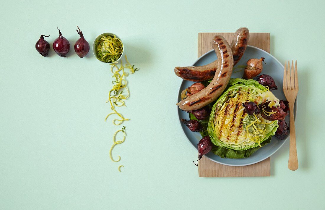 Grilled savoy cabbage with citrus and garlic butter, toasted onions and grilled sausages