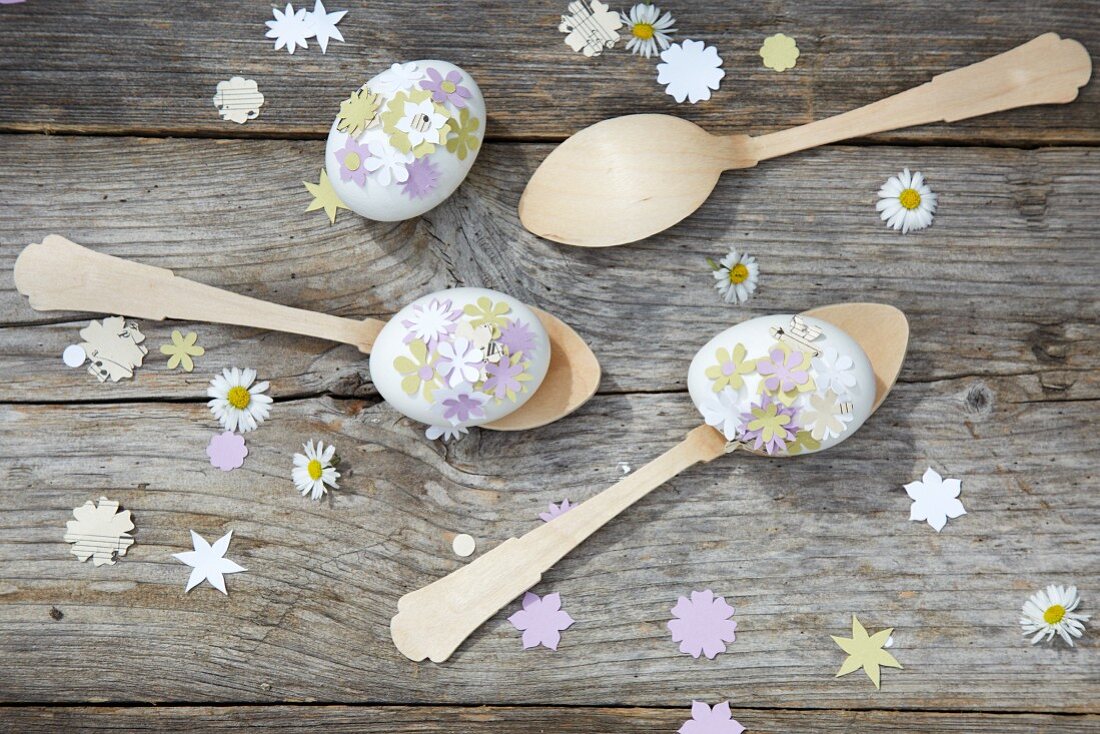 Mit ausgestanzten Blümchen verzierte Eier auf Holzlöffeln