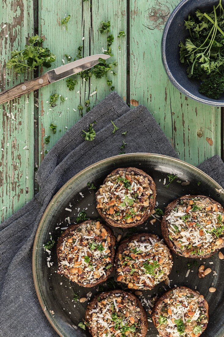 Portobello mushrooms stuffed with parmesan pine nuts garlic breadcrumbs and parsley on a green wooden table