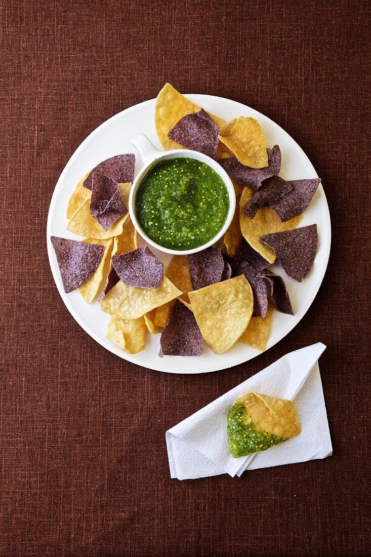 Verschiedene Tortillachips mit Tomatillosalsa auf Teller (Mexiko)