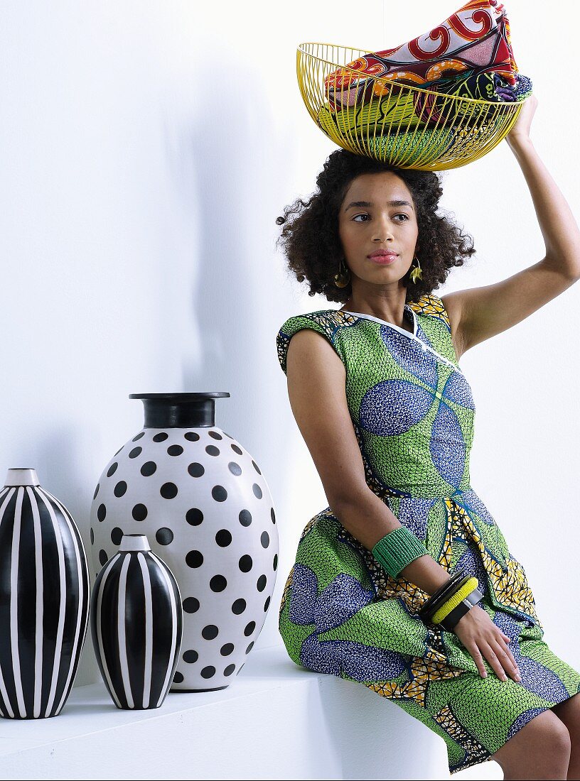 Young woman wearing ethnic dress holding wire basket next to black and white vases