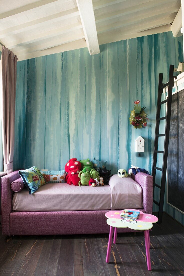 Soft toys on pink bed in front of turquoise wall in girl's bedroom with ladder leading to loft level on one side