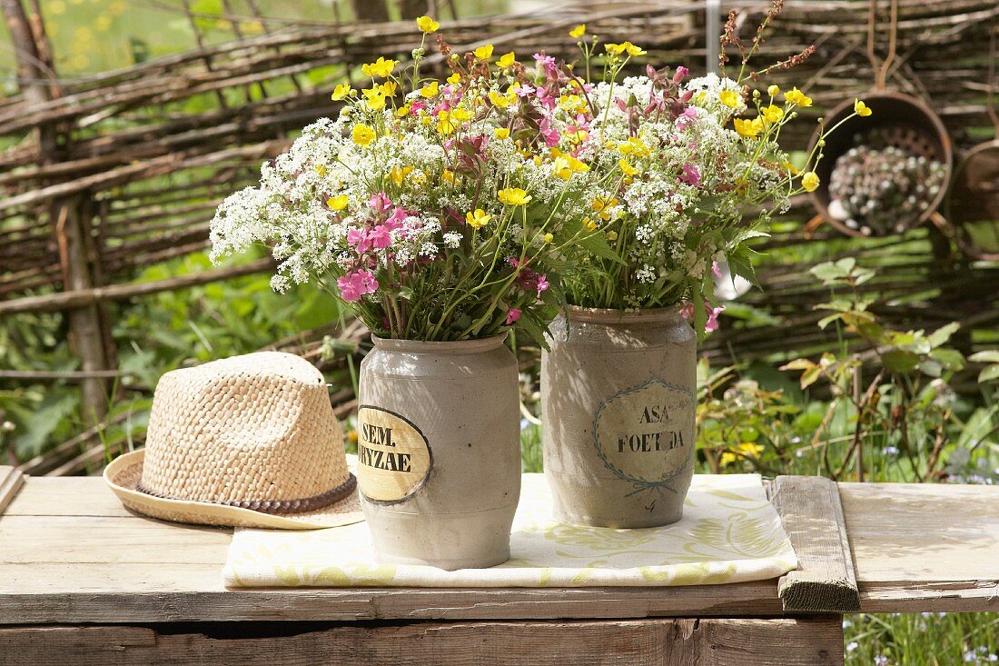 Bouquets of wild cow parsley, red campion and buttercups in two stone jars on garden bench