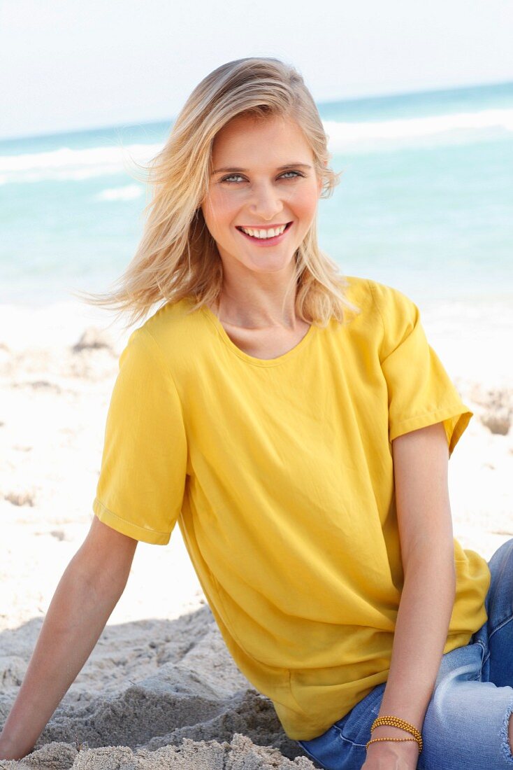 Blonde Frau in gelbem T-Shirt und Jeans am Strand