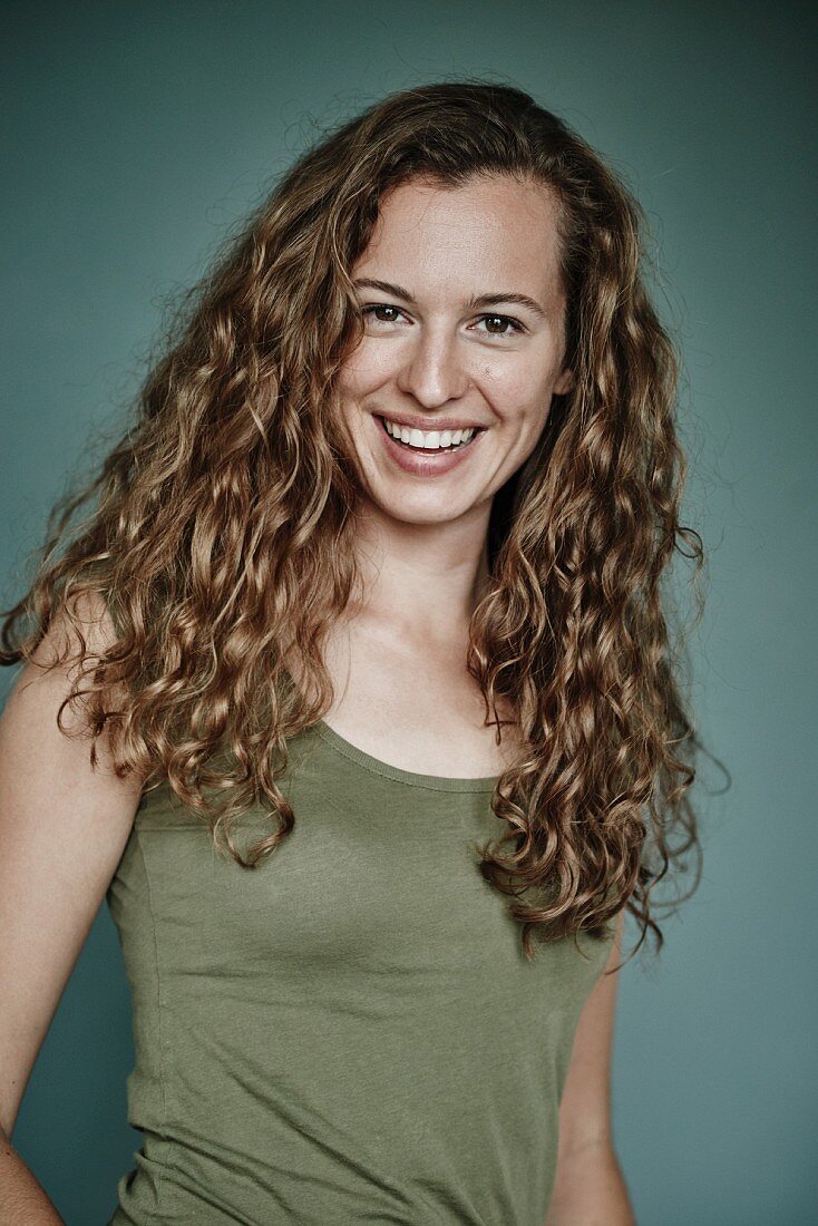 A brunette woman with curly hair, wearing a green vest top