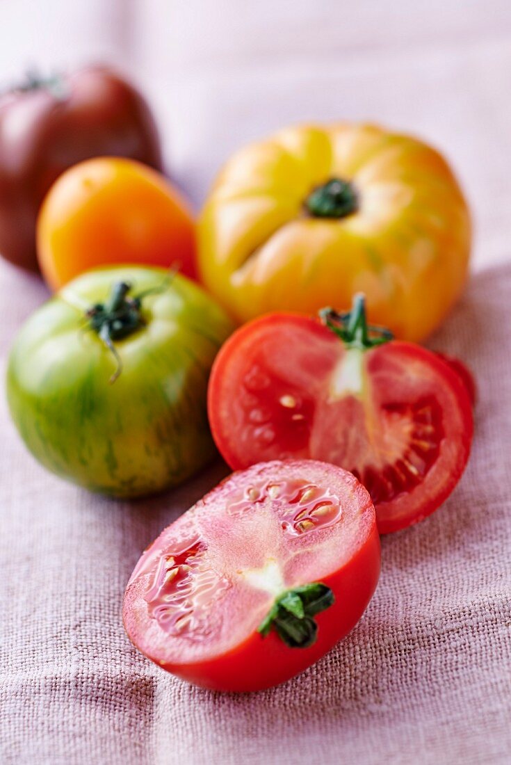 Verschiedenfarbige Tomaten auf Leinentuch, eine halbiert
