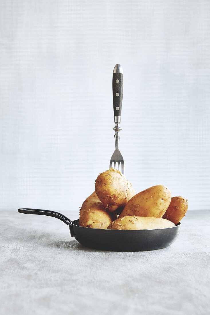A fork in raw, unpeeled potatoes in a frying pan