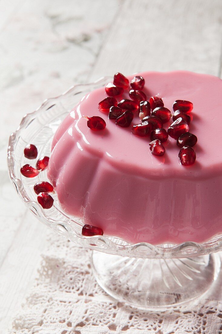 Pink Milk jelly covered in pomegrante seeds on a glass cake stand and vintage lace tablecloth