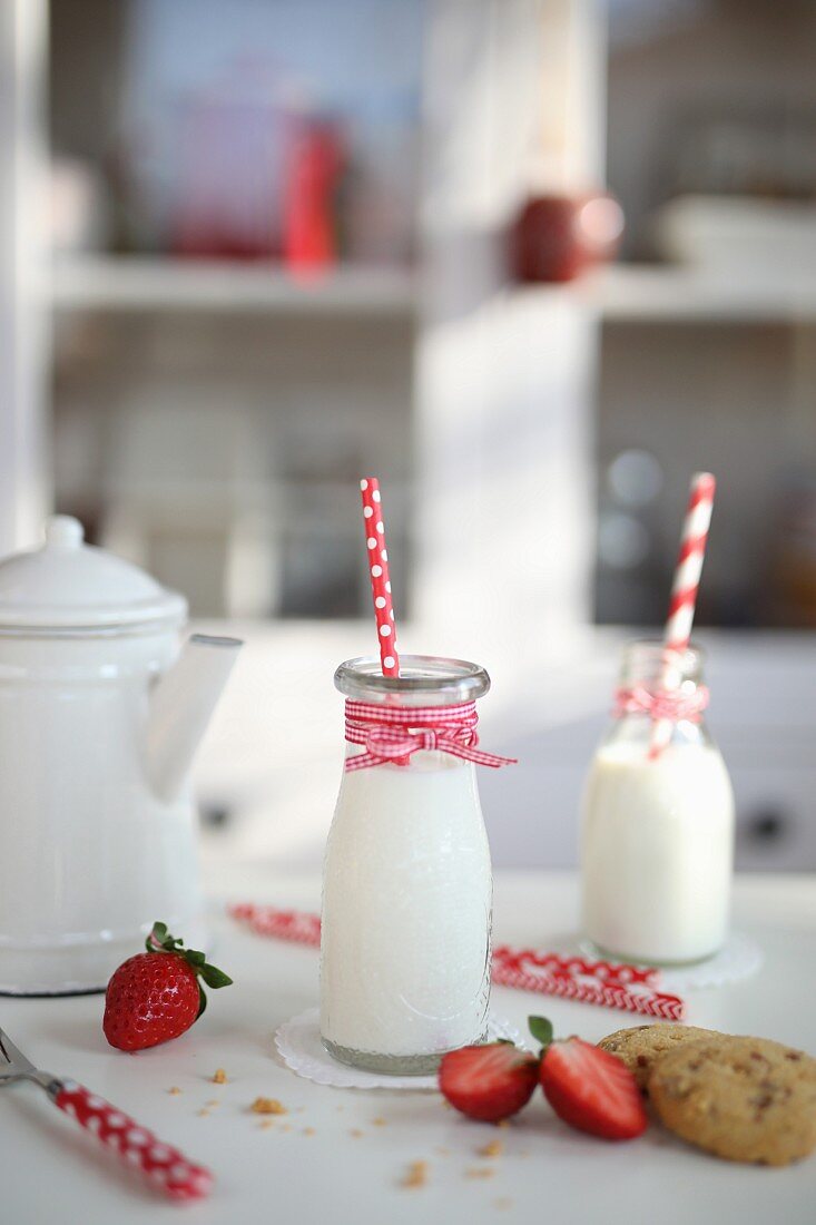 Milchflaschen, Erdbeeren und Cookies auf Küchentisch