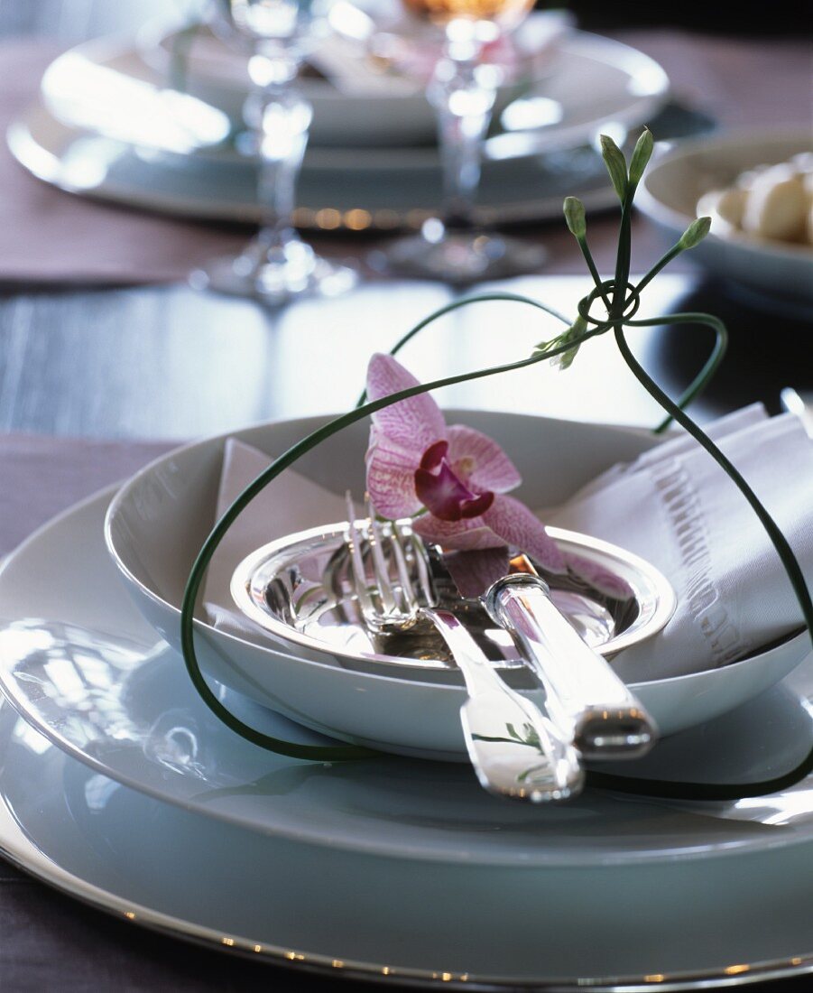 Elegant place setting with white crockery, silver cutlery and orchid flower