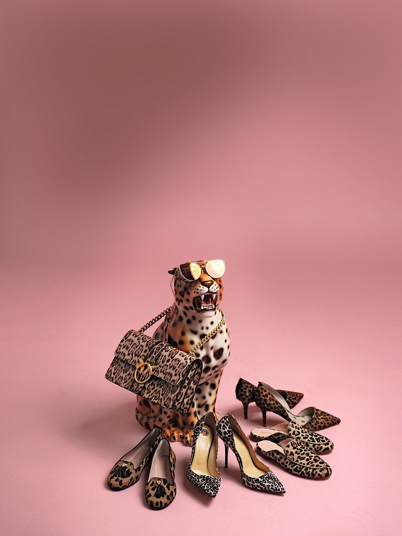A leopard figure wearing sunglasses and holding a handbag in its mouth, surrounded by various pairs of leopard-print shoes