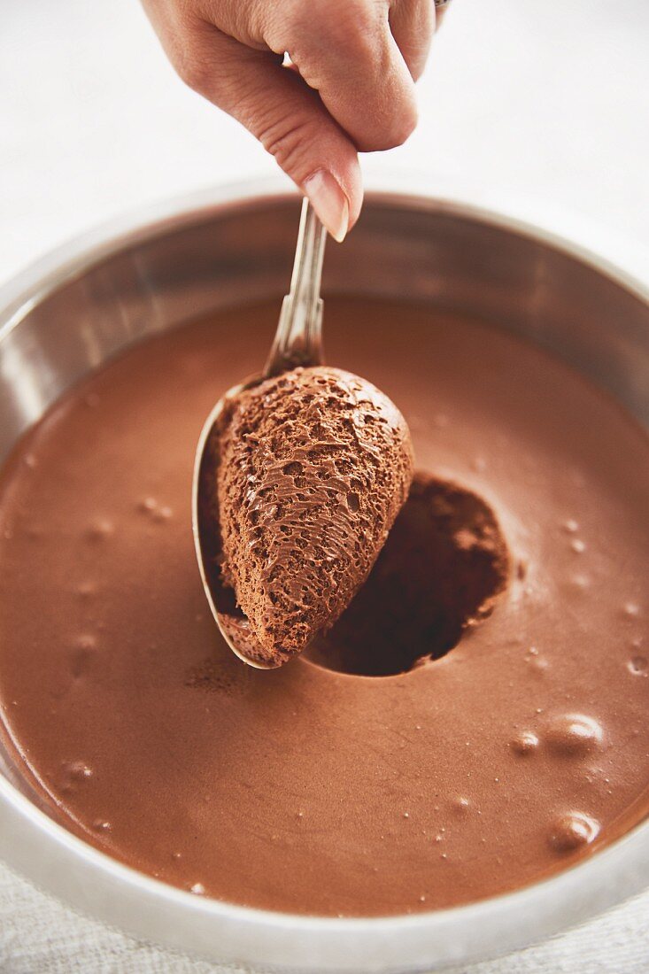 A quenelle of chocolate mousse being scooped out of a bowl with a spoon