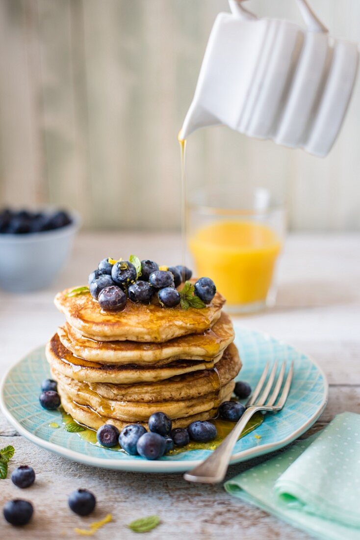 Gestapelte Pancakes mit Zitronenschale, Heidelbeeren und Ahornsirup zum Frühstück