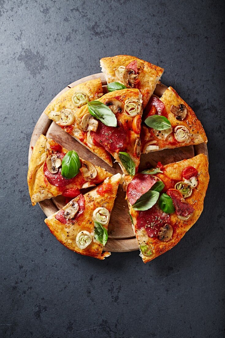 Pizza mit Pilzen, Salami und Lauch auf Schneidebrett