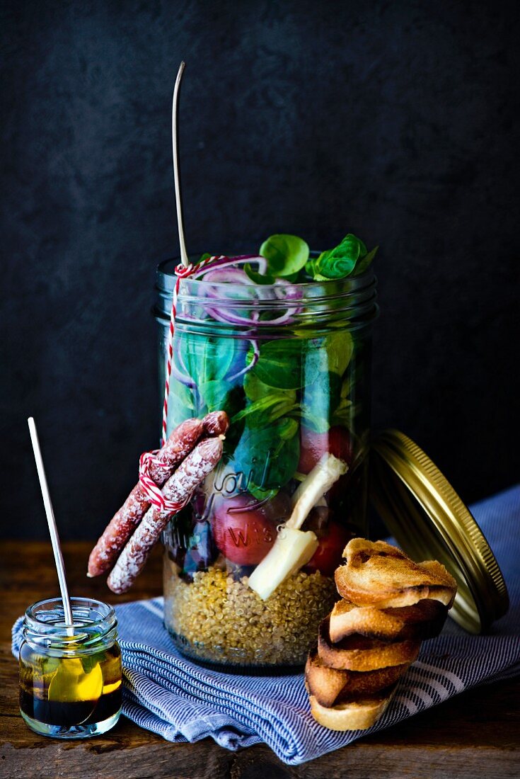 Lunch in a glass jar: quinoa salad, cherry tomatoes, lambs lettuce, black olives and goat's cheese and mini salami