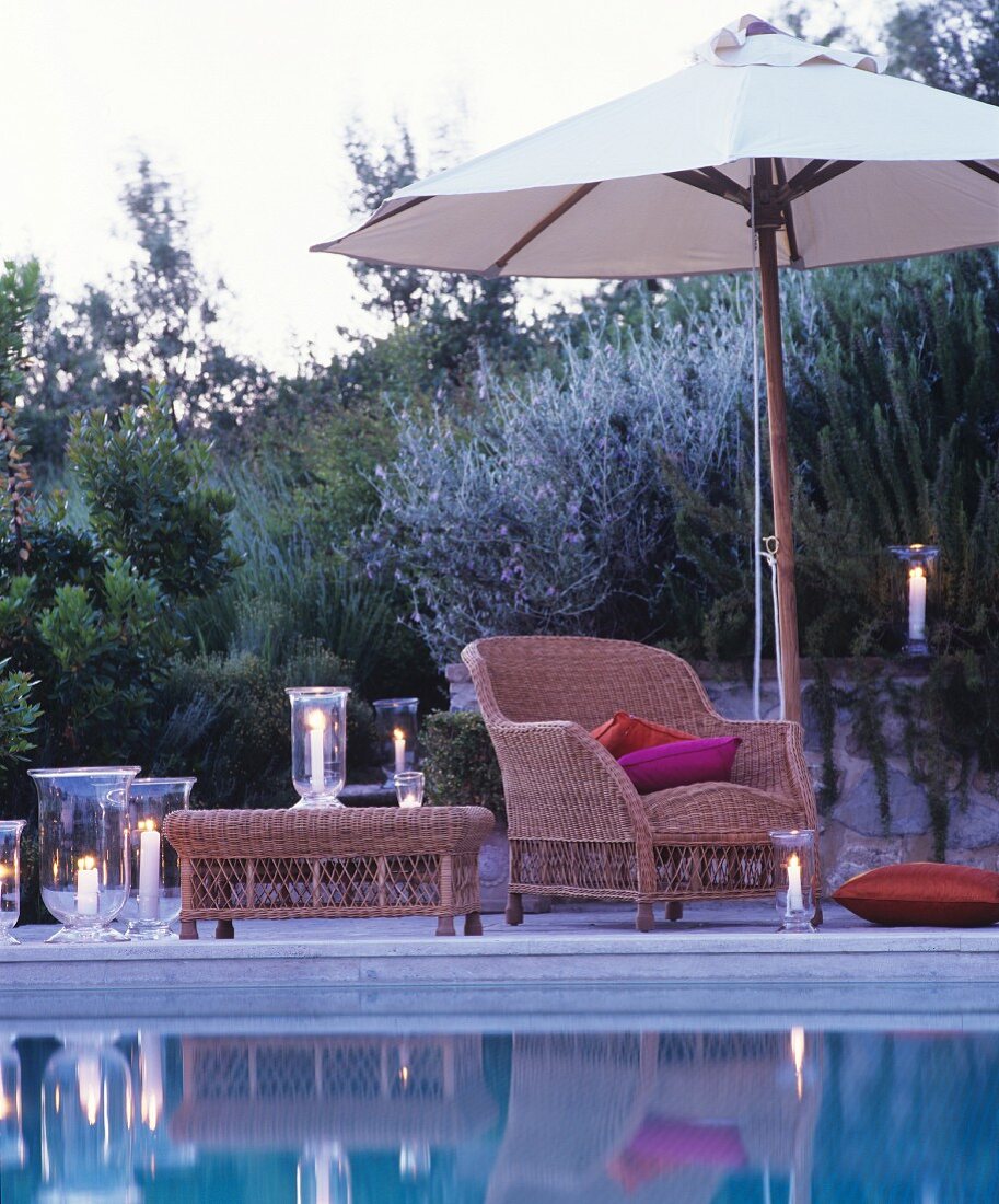 Romantic twilight ambiance: comfortable wicker armchair and lit candle lanterns next to swimming pool