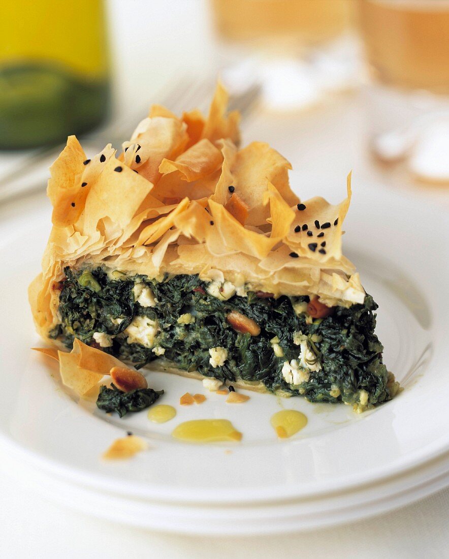 A slice of spinach filo pastry pie on a plate in a table setting