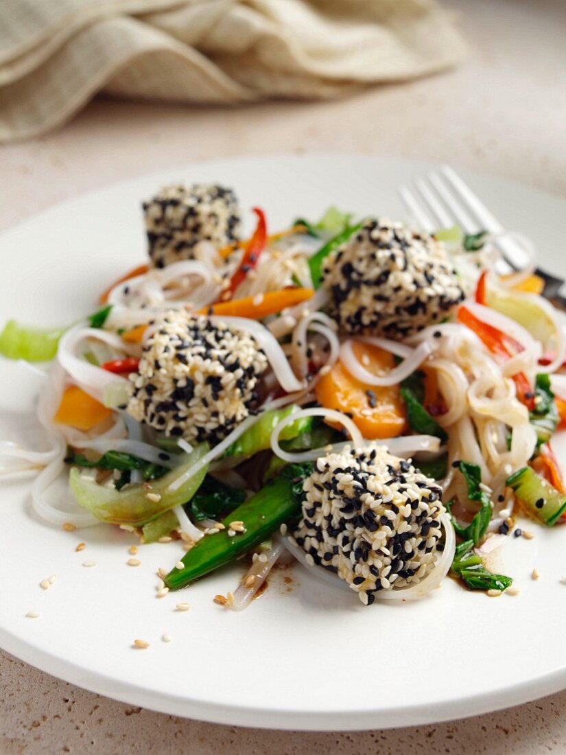 Deep fried tofu coated in black and white sesame seeds rice noodles stir fried vegetables carrots scallions sugar snaps
