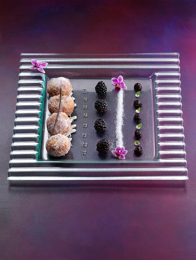 Mini-Donuts dekorativ arrangiert mit Beeren und Blüten auf Glasplatte