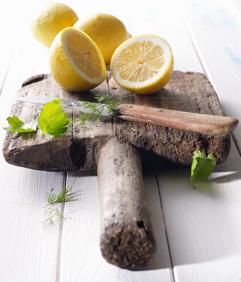 Halved lemons on an old wooden board with parsley, dill and a knife