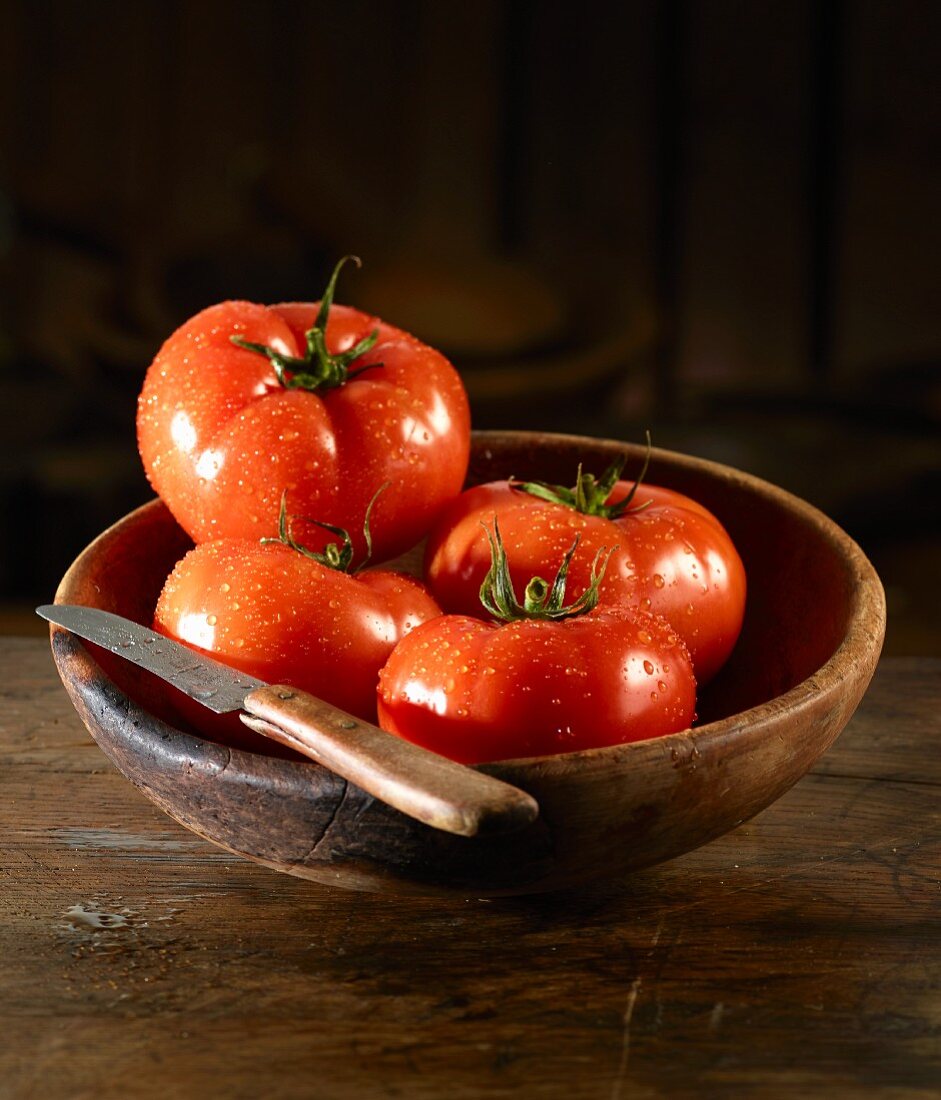 Tomaten mit Wassertropfen und Messer in einer Holzschale