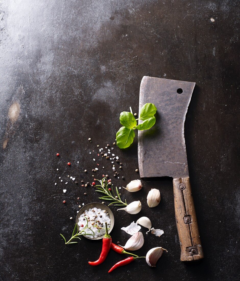 An old meat cleaver with garlic, salt, chilli and basil on a baking tray