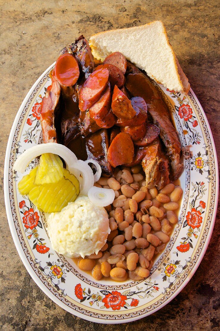 Barbecue ribs, sausage with beans mashed potatoes white bread onion and pickle cucumber, Texas, USA