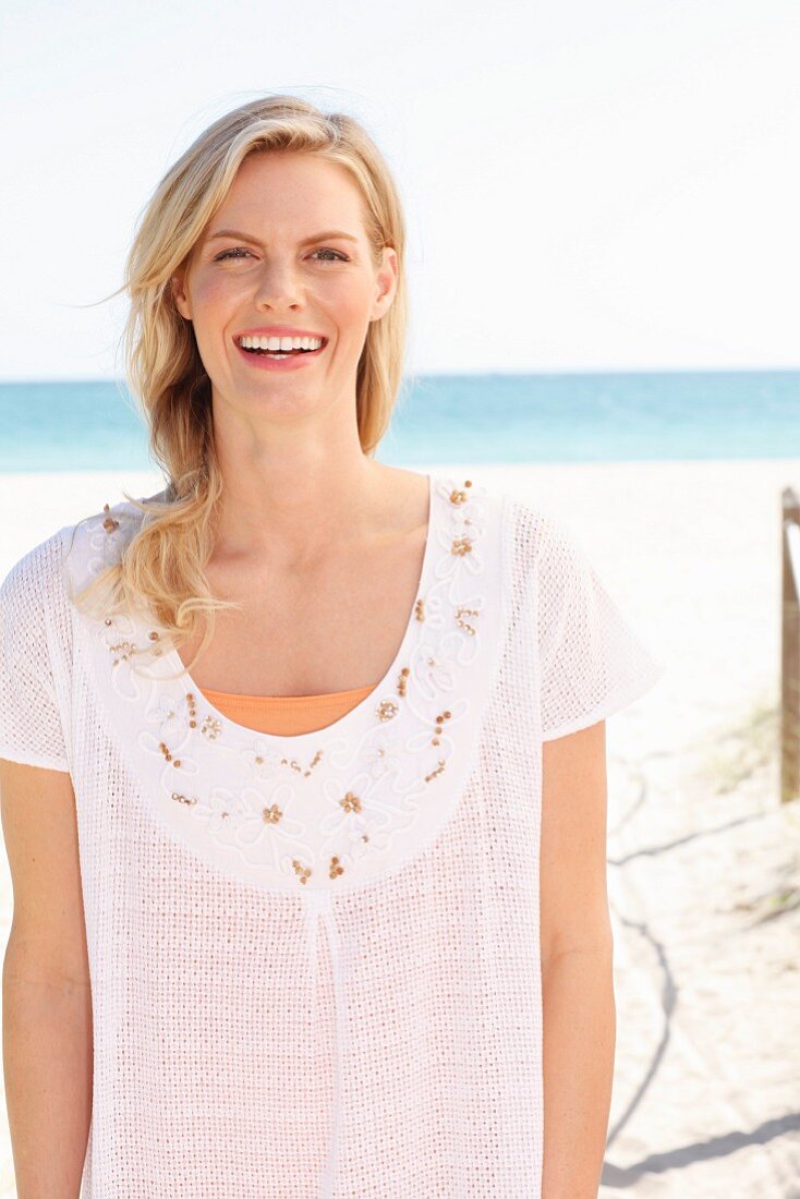 Blonde Frau in weißem T-Shirt mit Stickerei am Strand