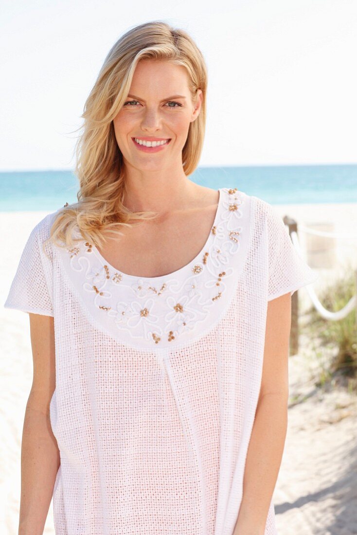 Blonde Frau in weißem T-Shirt mit Stickerei am Strand