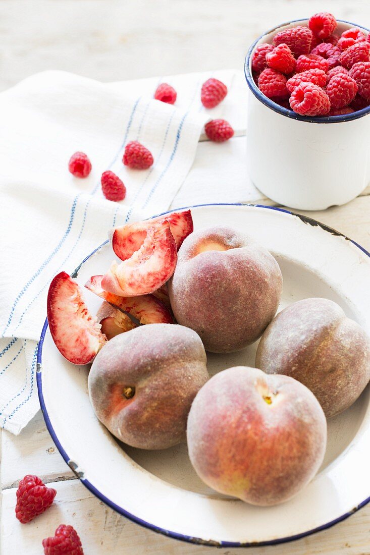 Red vineyard peaches and fresh raspberries in enamel dishes