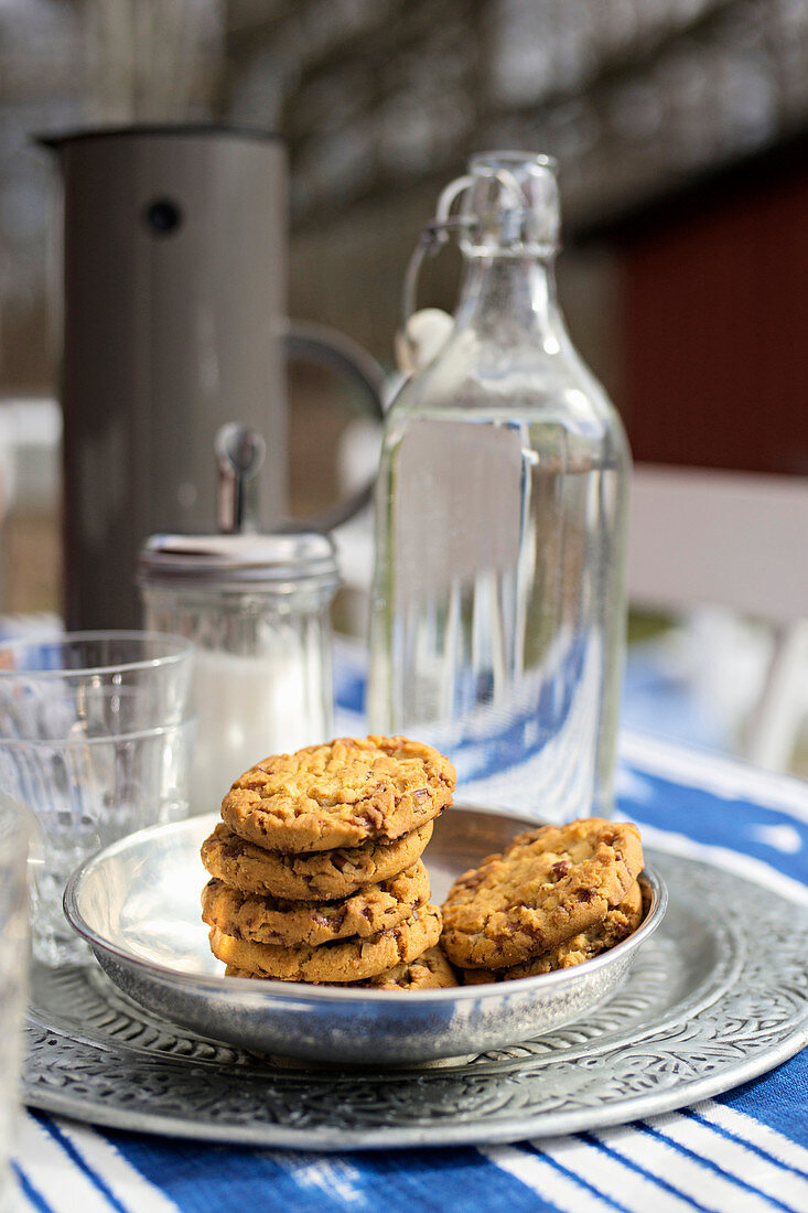 Plätzchen in silberne Schale und Bügelflasche auf Gartentisch