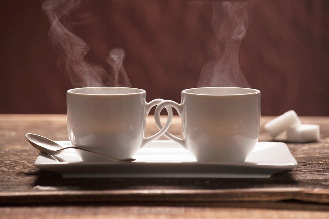 Two steaming coffee cups with interlocking handles