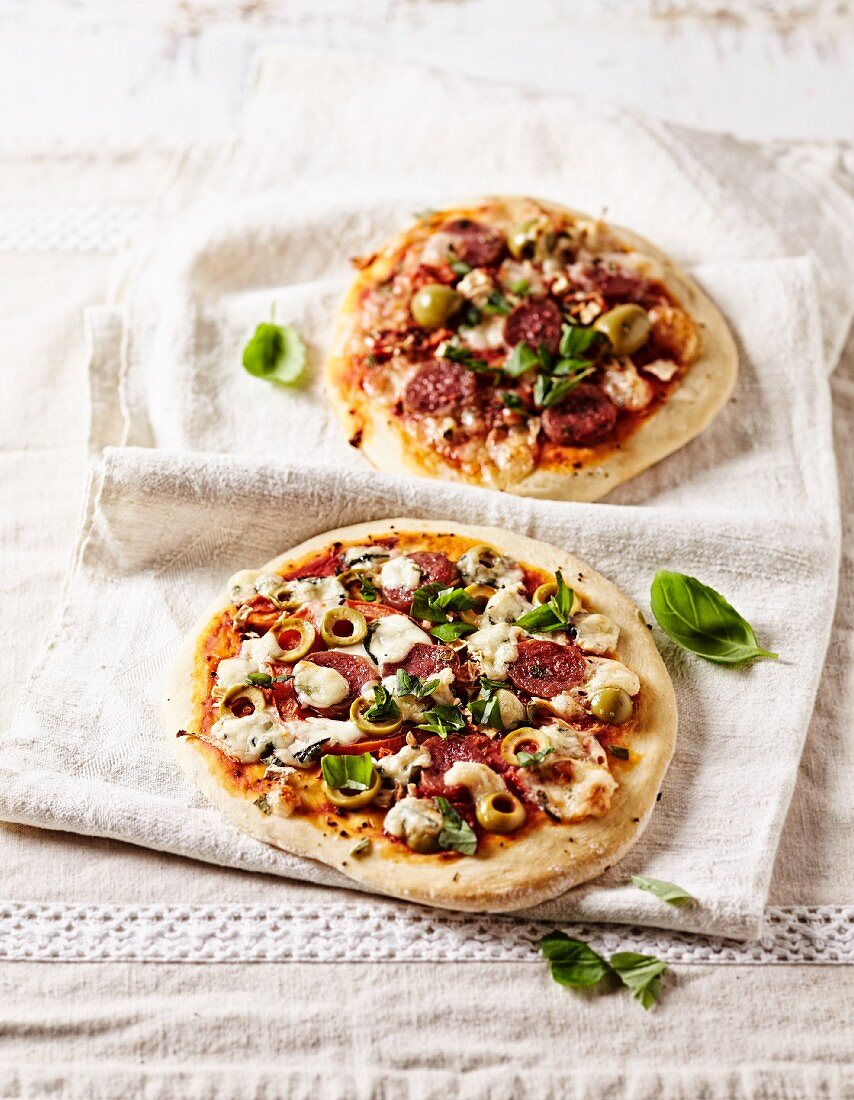 Zwei rustikale Pizzen mit Chorizo, grünen Oliven und Basilikum