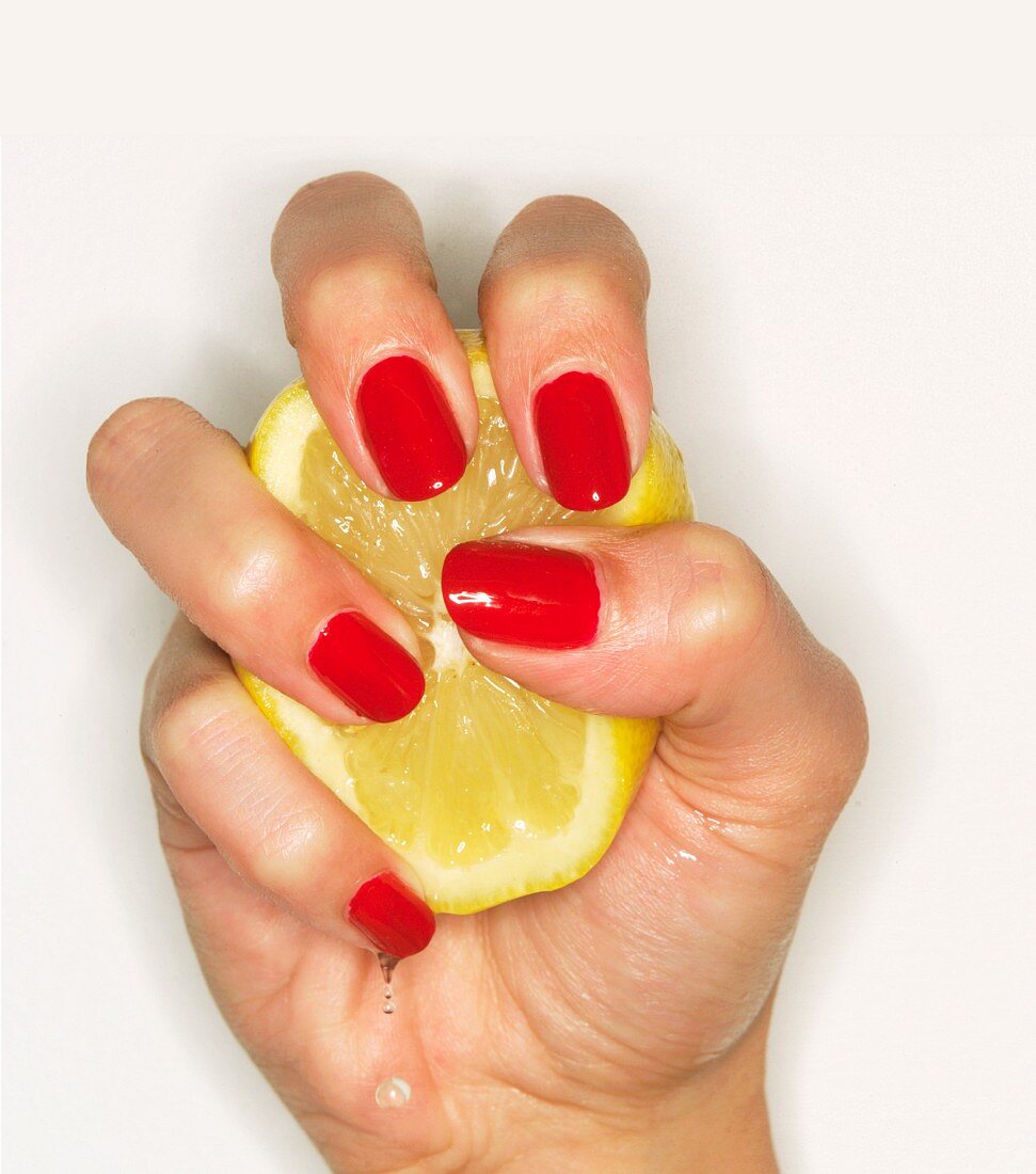 Frauenhand mit rot lackierten Fingernägeln quetscht Zitronenhälfte