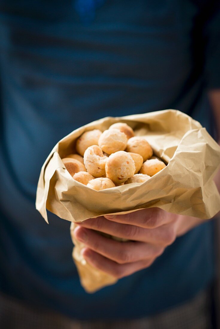 A hand holding a paper bag of crunchy ball-shaped snacks
