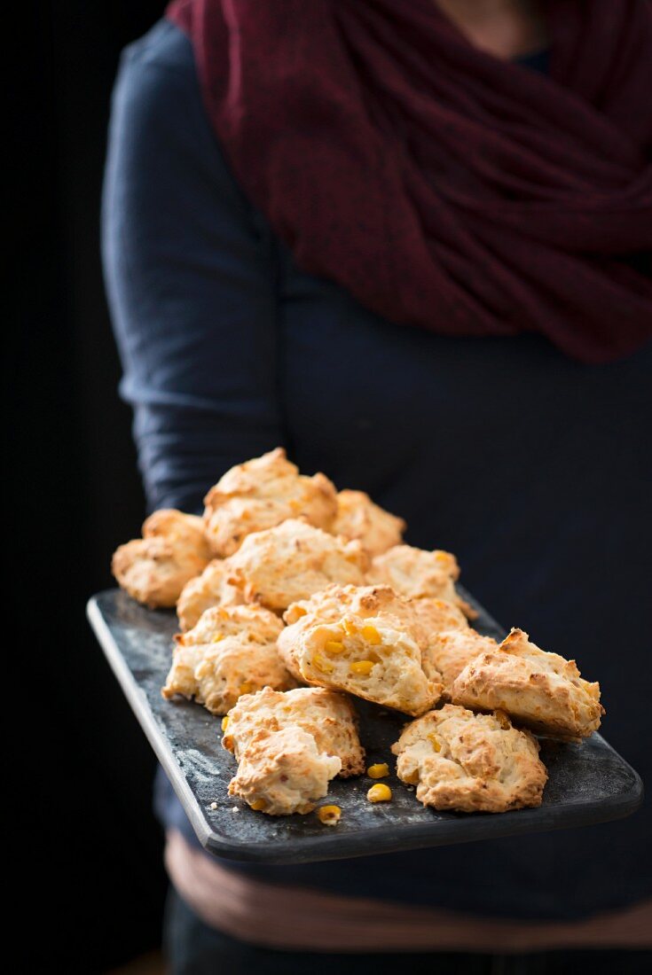 A woman serving corn biscuits on a wooden chopping board