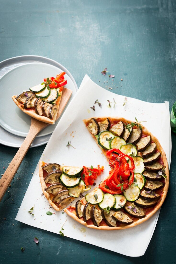A ratatouille tart on baking paper with a slice cut out